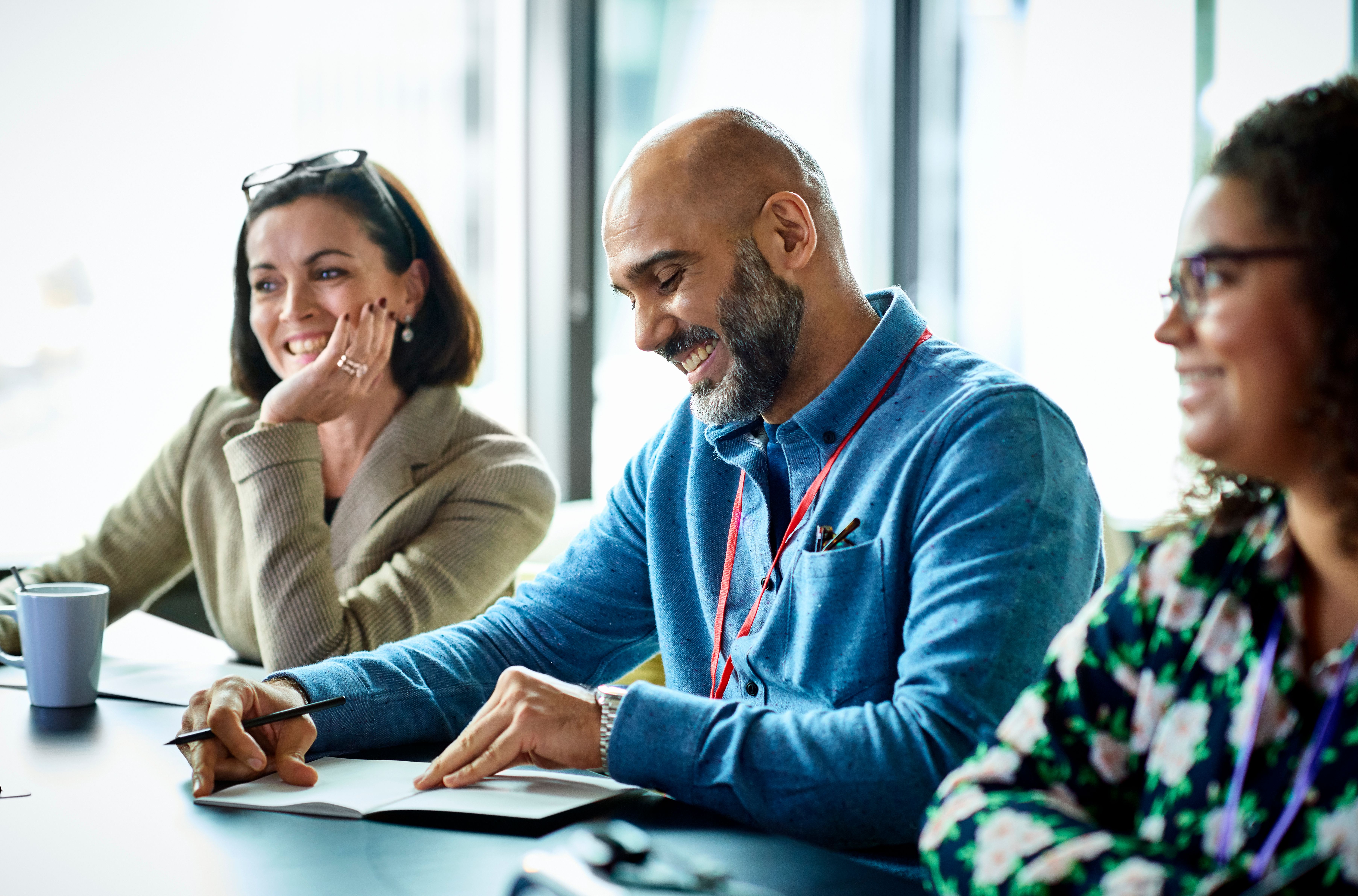 A man and two women colleagues smile during a meeting in a modern office conference room