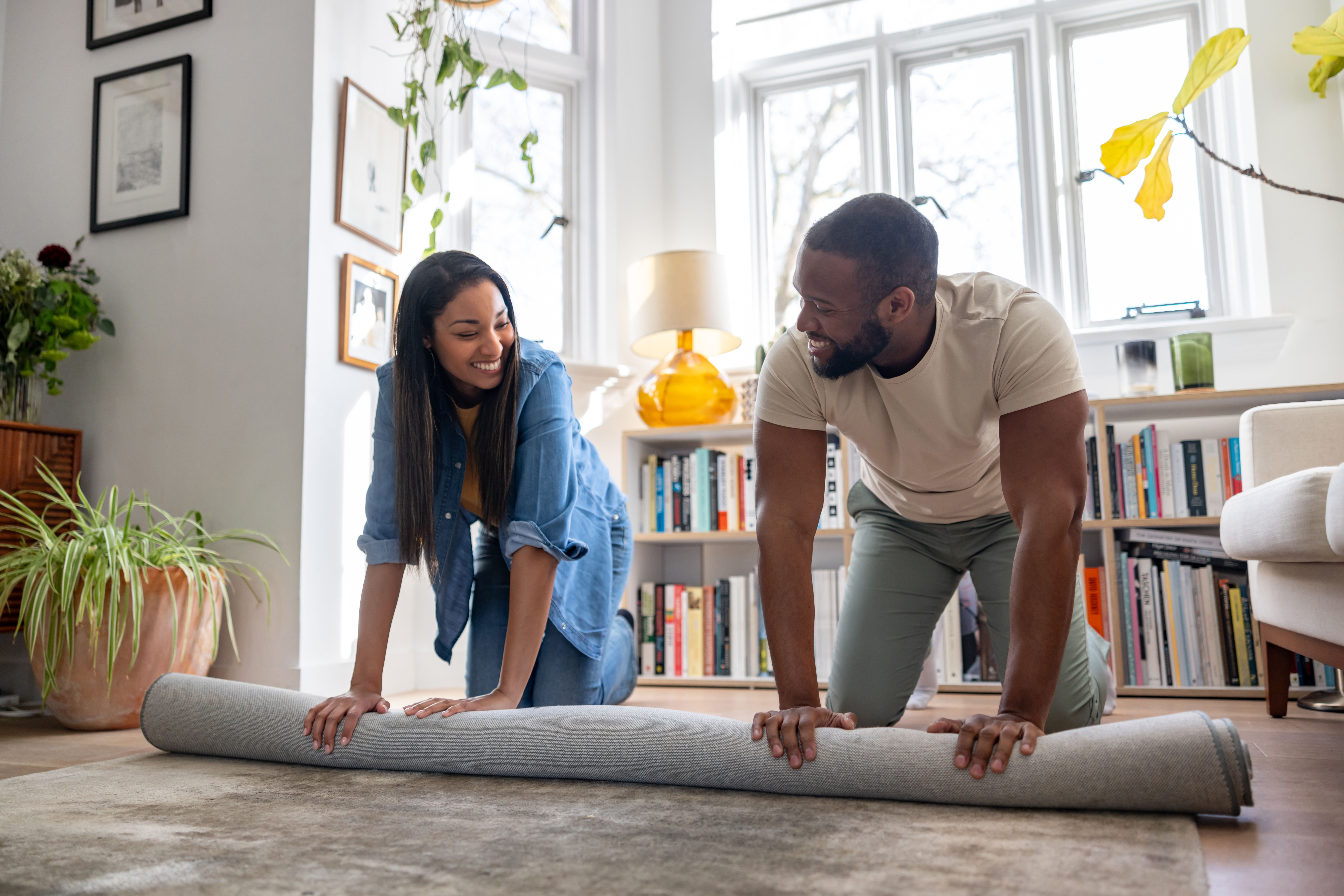 A couple unrolling a rug in a bright living room.