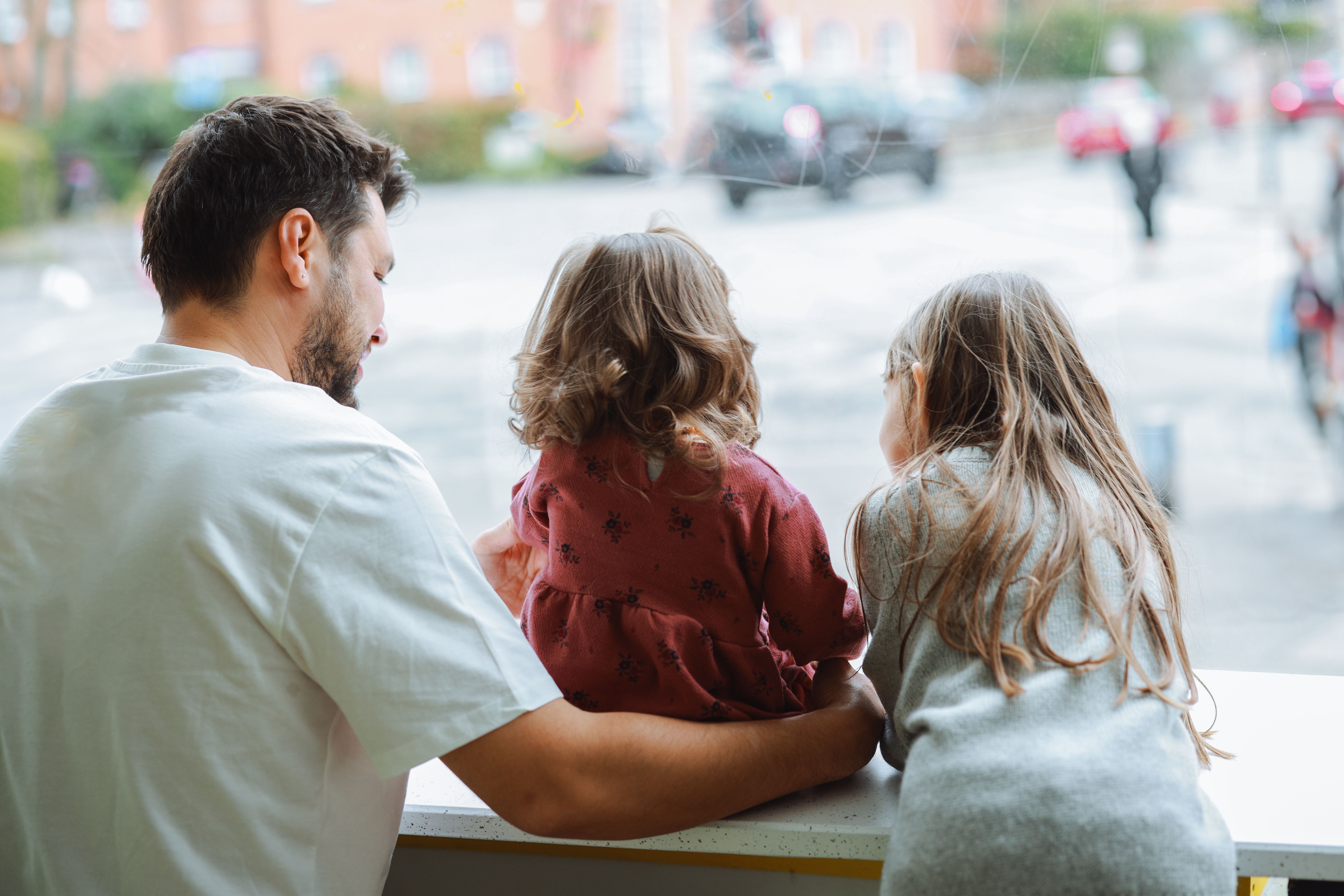 A parent sitting with two children, looking out a window together.