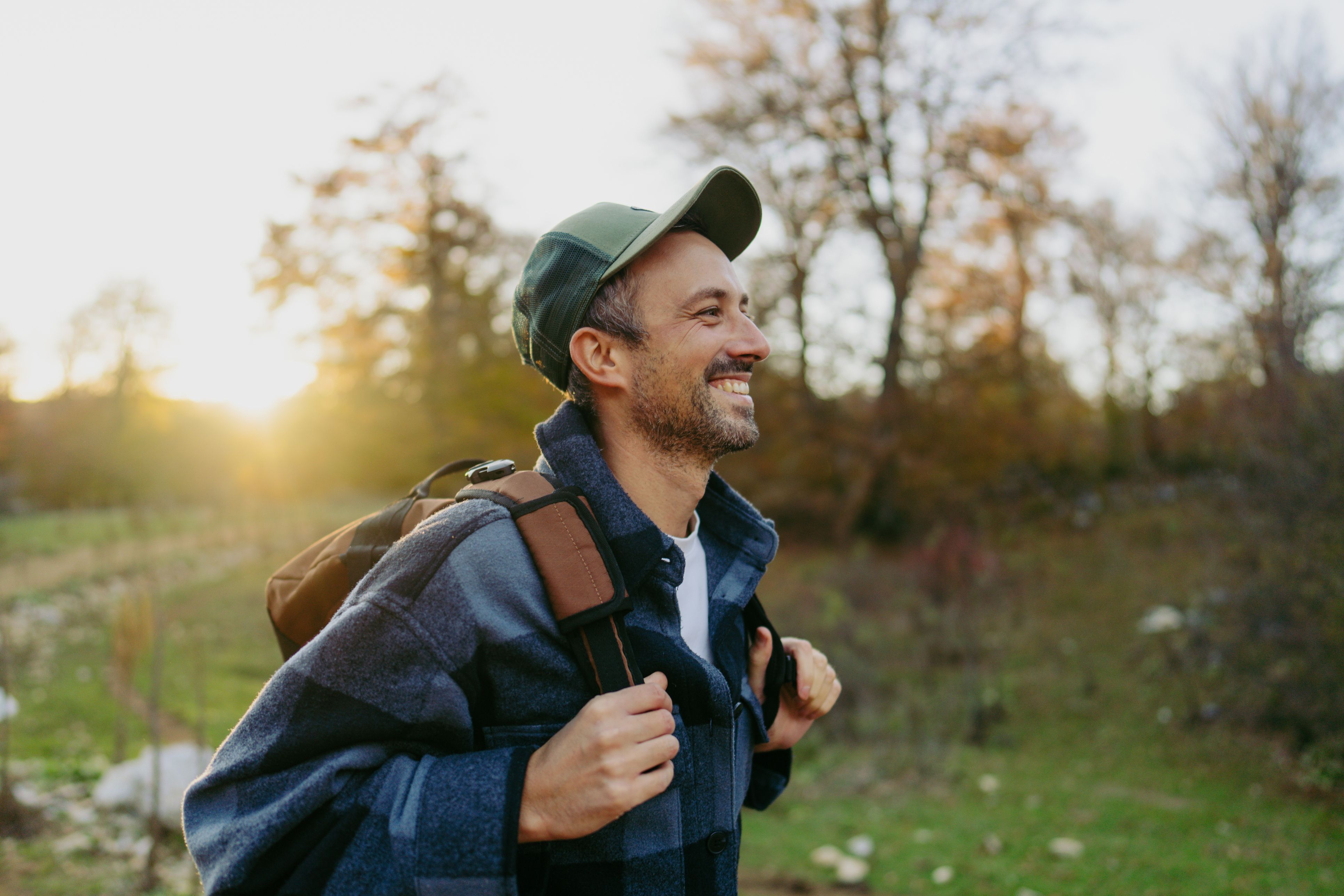 A man is enjoying a walk in a green park, smiling as the sun rises in the background.