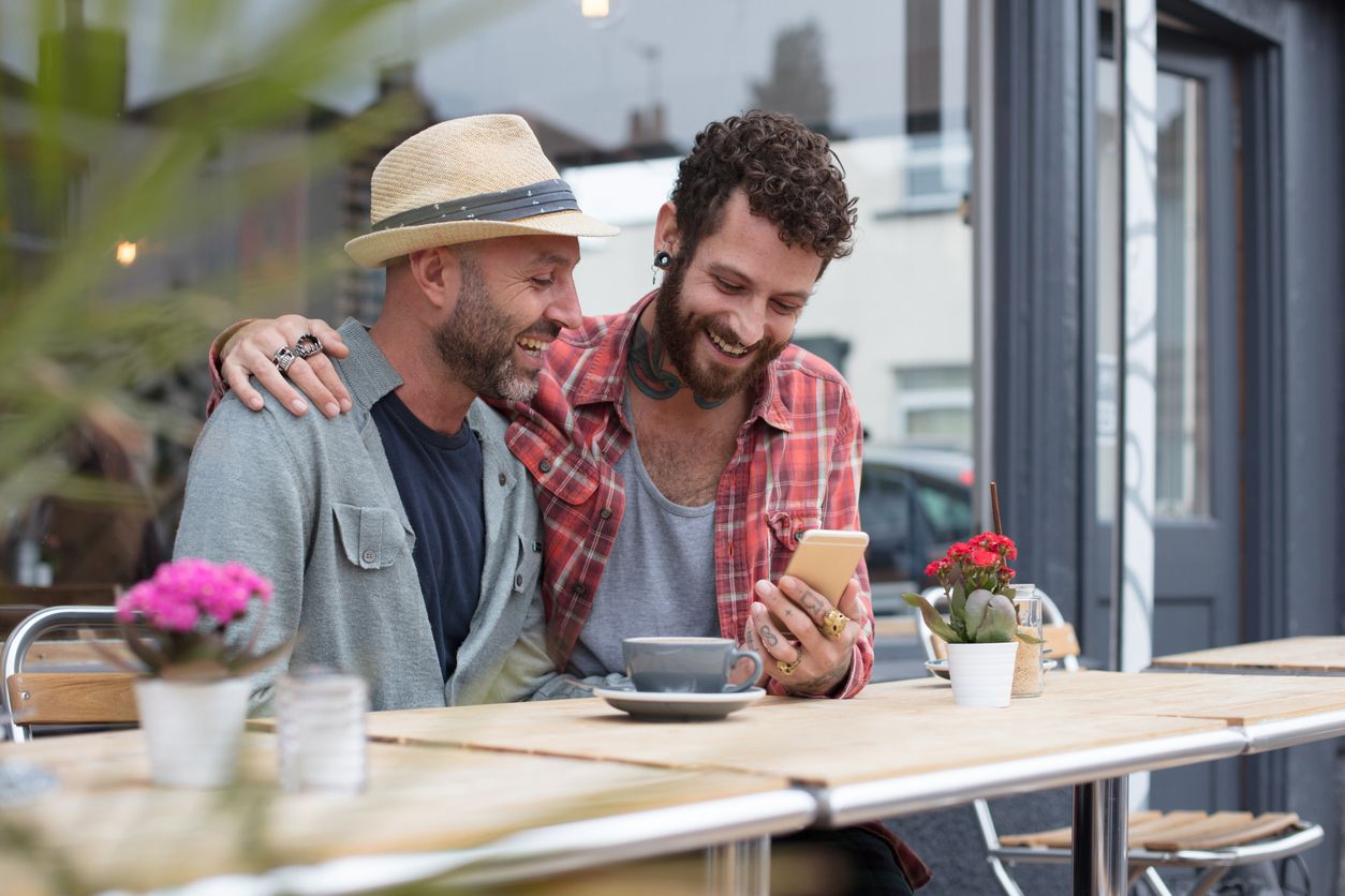 Two friends smiling and looking at a phone at an outdoor café.