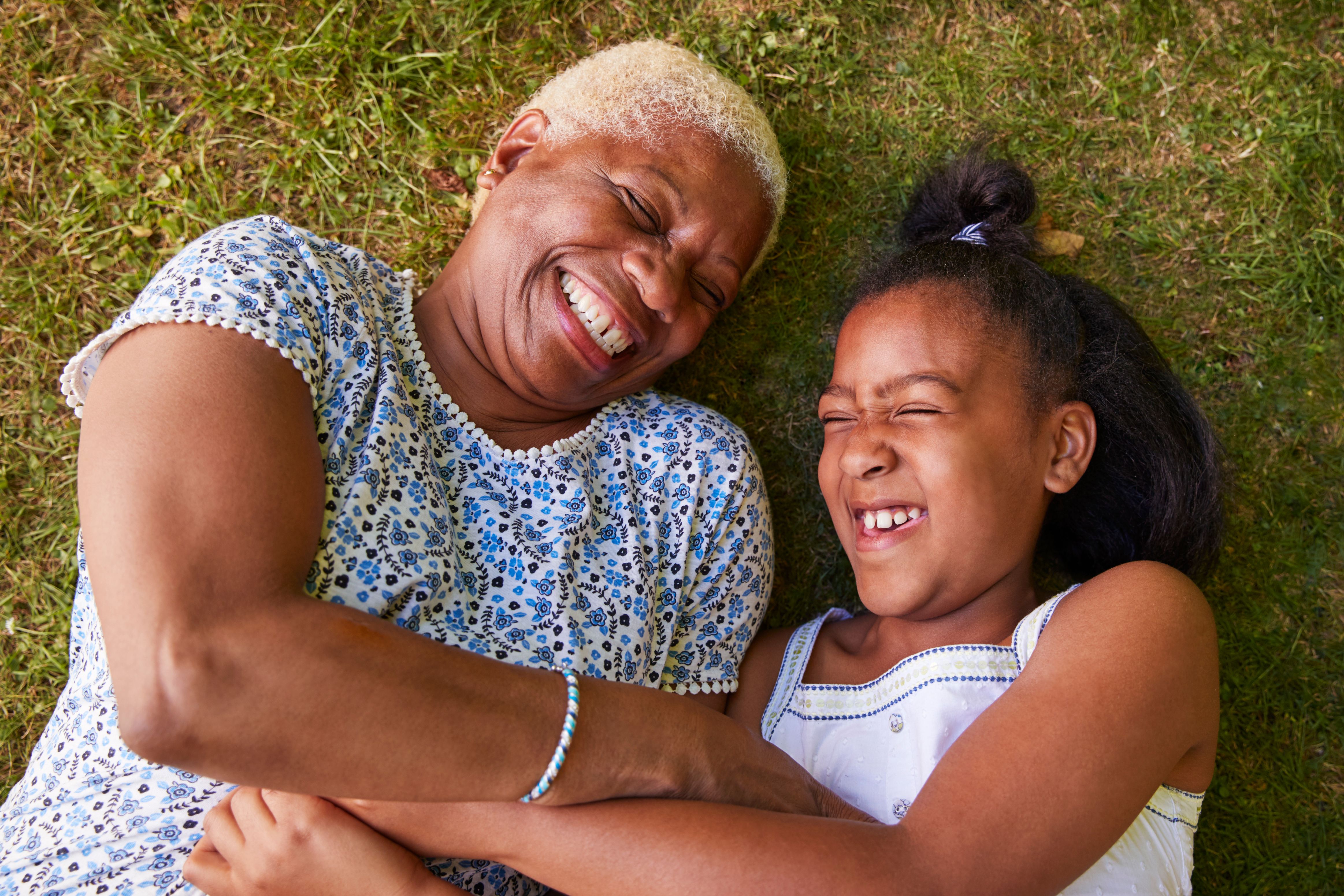 Grandmother and granddaughter lying on the grass in the sunshine, smiling together.