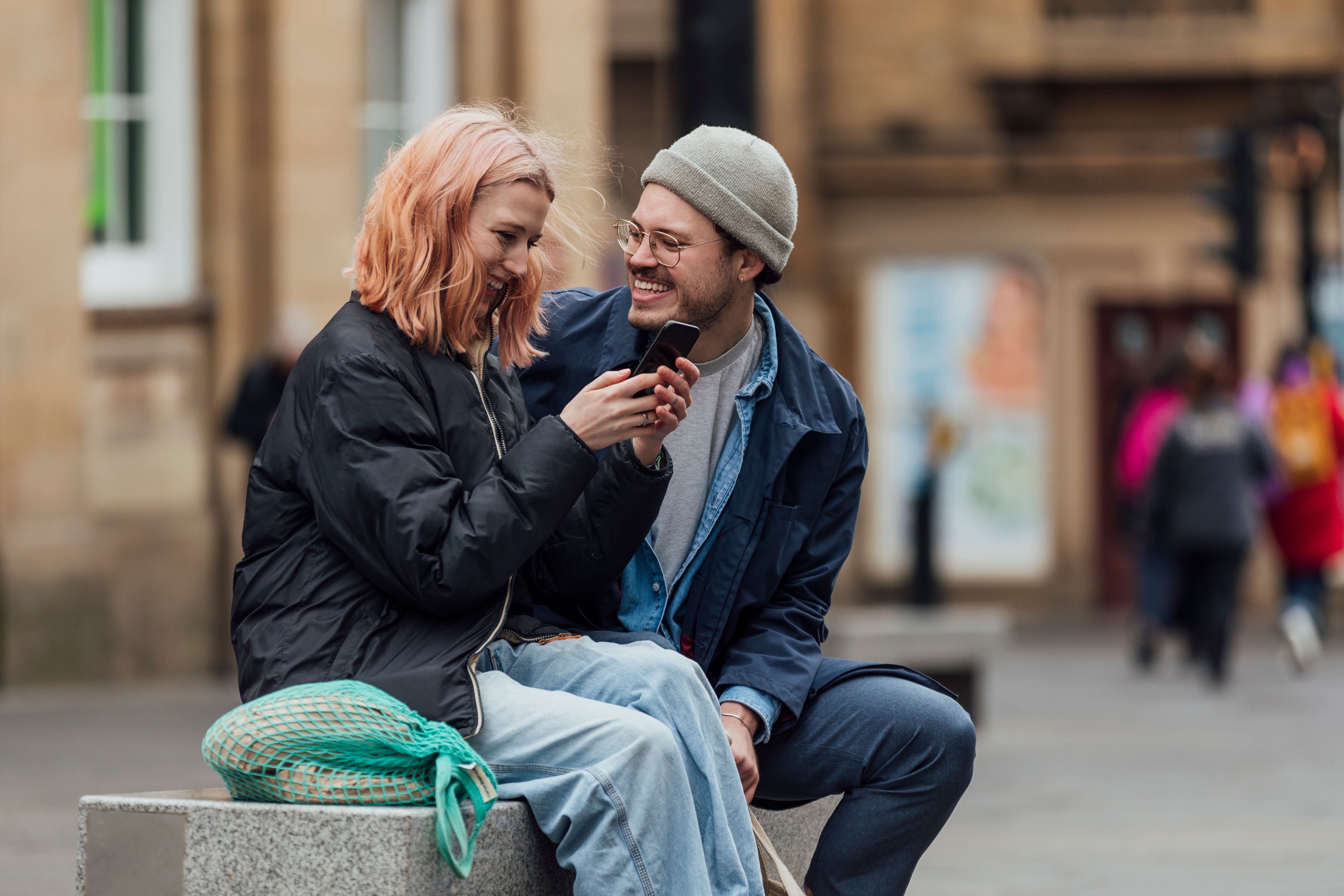Young couple sitting on a bench on the road, smiling.