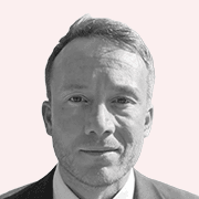 A black and white headshot of Chris Mooney, smiling at the camera against a plain, light-coloured studio background.