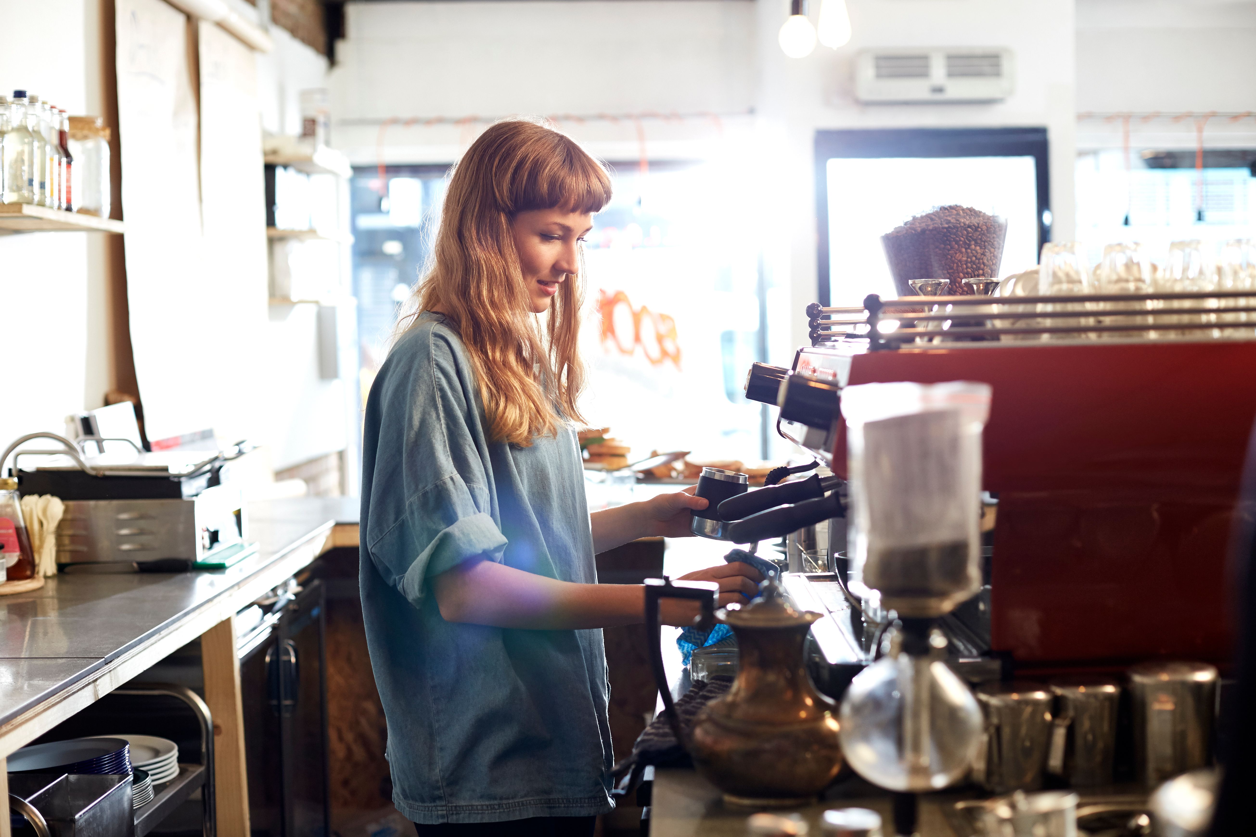 A smiling woman prepares coffee behind the counter of a coffee shop