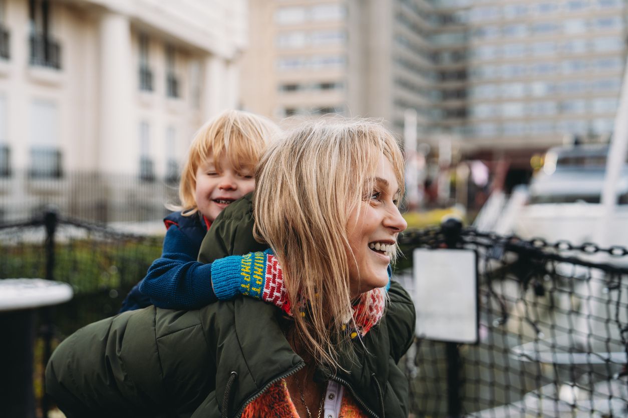 Over-50 grandmother smiling while carrying her grandchild outdoors.