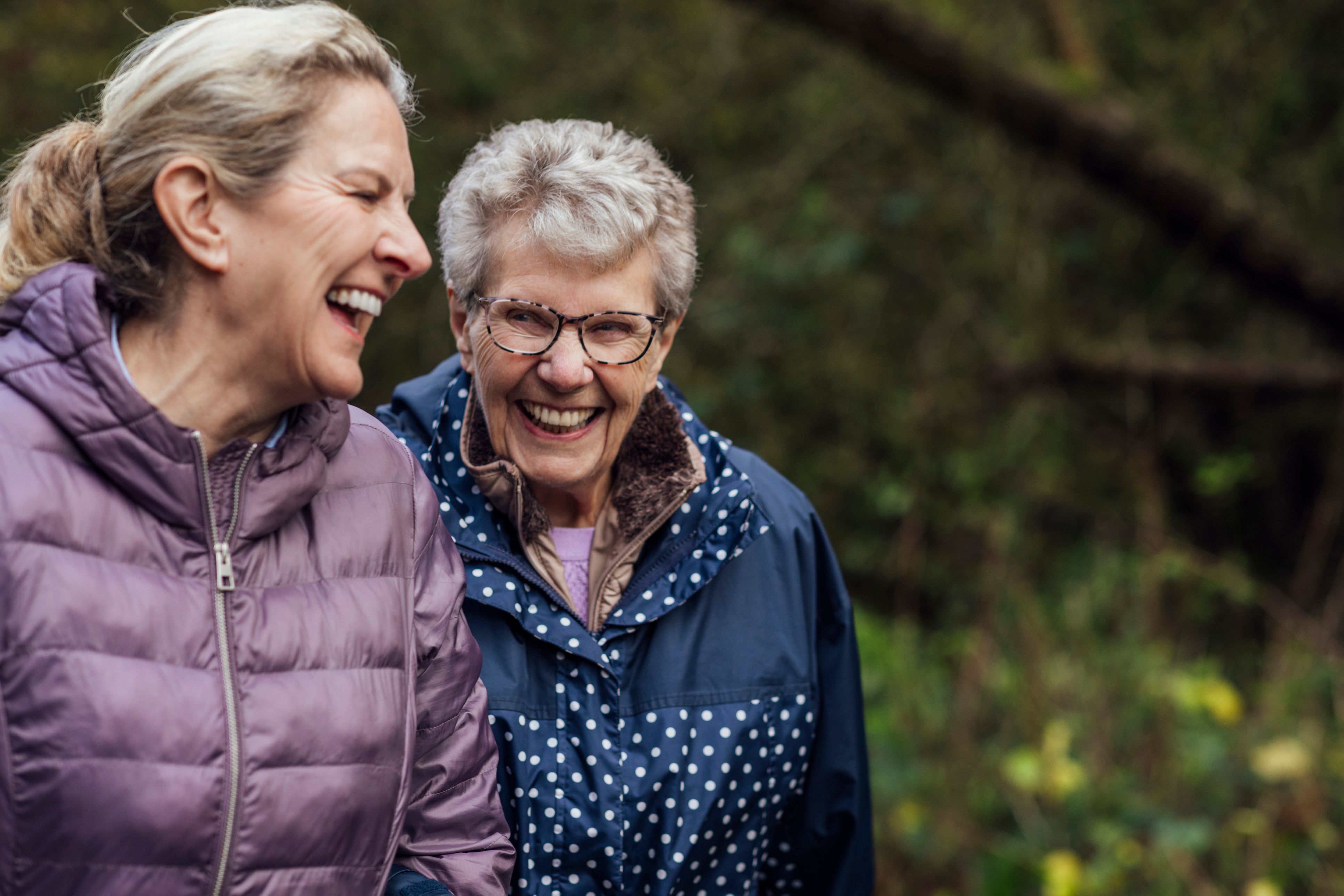 A young woman and her mother laughing while walking through a park