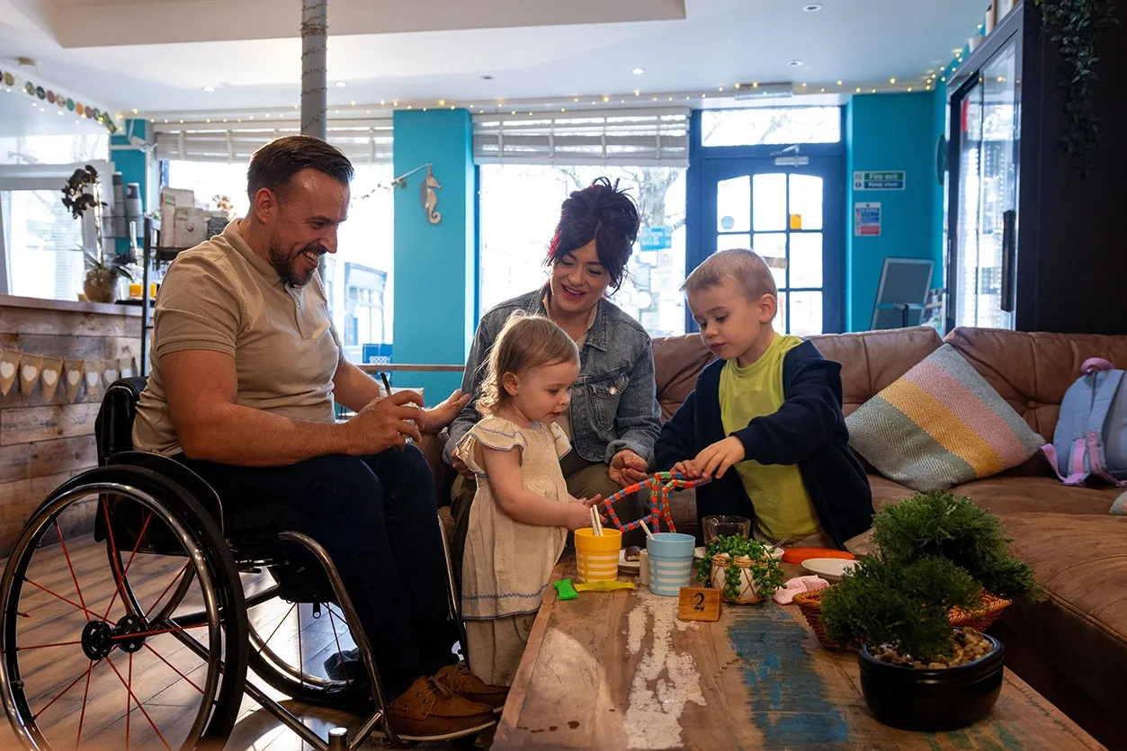 Family in a coffee shop with two kids and man in wheelchair. 