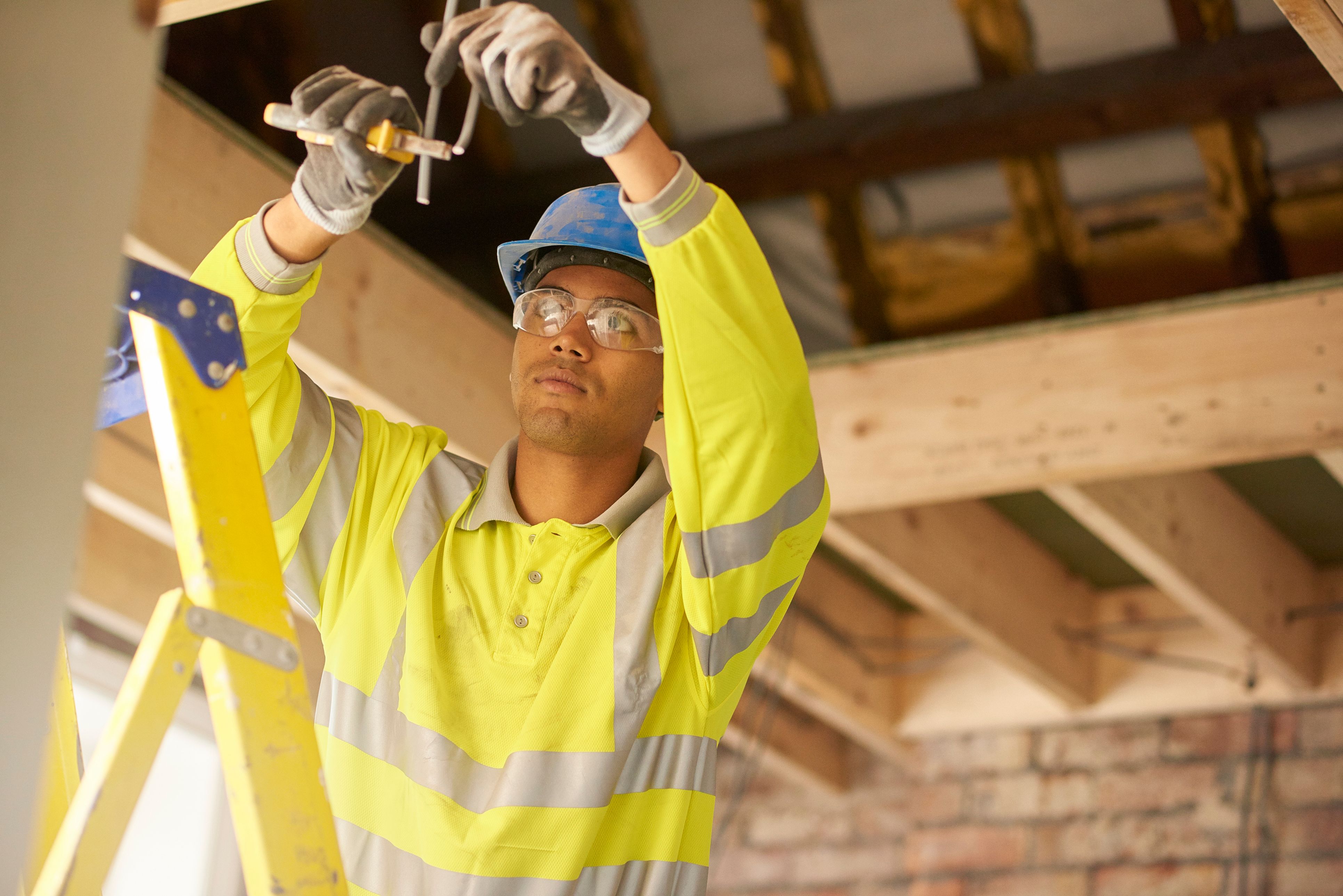 A man working on a building site, wearing a high-vis jacket and a hard hat, cutting wires. 